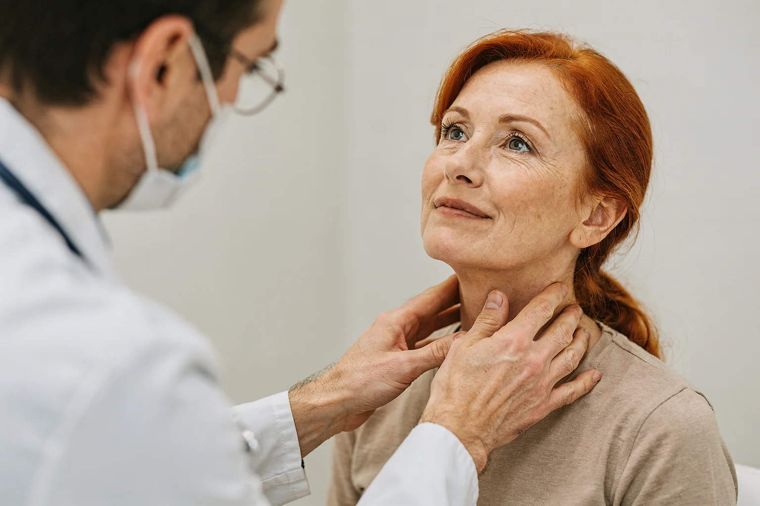 A physician gently examines a patient's neck during a thyroid physical exam